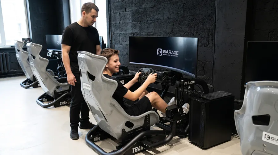Администратор клуба Garage настраивает гоночный симулятор под подростка перед заездом